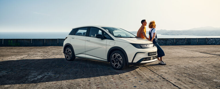 BYD karbantartás: fehér BYD Dolphin parkol a tengerparti betonplaccon, mellette egy pár